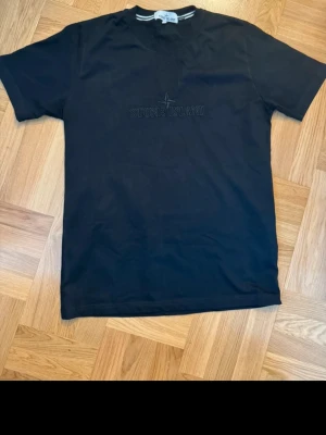 Svart S.I t-shirt i bomull - Snygg svart t-shirt med diskret broderad logga på bröstet. Klassisk passform och rund halsringning. Tillverkad i mjuk bomull som känns skön mot huden. Perfekt till jeans eller shorts för en clean och stilren look.