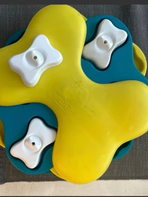 Gul och blå aktiveringsleksak för hund - Rolig aktiveringsleksak för hund från Nina Ottosson i plast. Leksaken är gul och blå med vita benformade lock som hunden kan flytta på för att hitta godis. Perfekt för att stimulera hundens hjärna och motverka tristess.