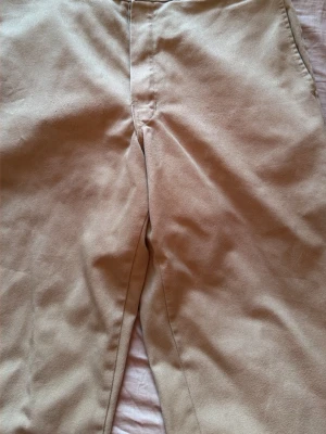 Beige chinos från Dickies - Snygga beige chinos från Dickies med klassisk rak passform. Byxorna har diskreta bakfickor och är tillverkade i ett slitstarkt bomullsmaterial. Perfekta för en clean och stilren look. Lite sönder där vid fötterna men klipp av de som är sönder så är de fantastiska 