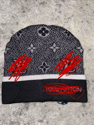 Svart mössa med monogrammönster - Snygg svart mössa med vitt monogrammönster och en bred vit rand längst ner. Mössan har en avslappnad passform och är stickad i mjukt material. Perfekt accessoar för att lyfta din outfit under kalla dagar.