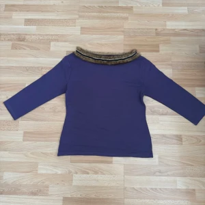 Lila topp med fuskpälsdetalj - Trendig lila topp med trekvartsärm och en unik krage dekorerad med brun fuskpäls. Toppen har en rak passform och är perfekt för dig som vill sticka ut med en cool detalj. Materialet känns mjukt och stretchigt. Storlek xl men förminskad som m, bröst 100-104cm.