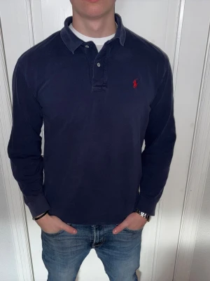Mörkblå långärmad piké från Ralph Lauren - Mörkblå långärmad piké från Ralph Lauren i storlek M.  Fint skick till ett bra pris. Nypris: 1995kr. Mitt pris: 349kr. Vid frågor eller funderingar, tveka inte att höra av dig.