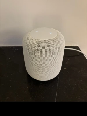 Vit Apple HomePod smart högtalare - Säljer en vit Apple HomePod, en smart bärbar högtalare med rundad cylinderform och mesh-tyg runt om. Touchpanel på ovansidan med LED-belysning för styrning. Perfekt för musikstreaming och smarta hemmet. Snygg och modern design som passar in överallt.