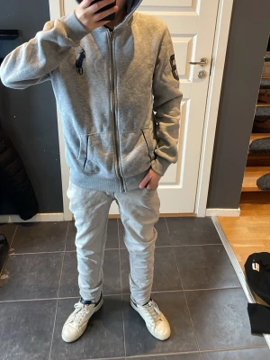 Grå zip hoodie från Ralph Lauren - Snygg grå hoodie med dragkedja från Ralph Lauren. Klassisk design med stor broderad logga på bröstet och patch på ärmen. Utrustad med huva och två fickor framtill. Perfekt för en avslappnad och stilren look. Storleken är XL för barn/ 14-17 år. Längden från botten av tröjan upp till axeln är ca 64 cm och axelbreden är ca 43 cm lång. Ny pris är mellan 1200- 2000kr men hör får du för en mycket billigare peng, i ett mycket bra skick, Skulle säga i ett 8,5/10. Tar emot bud