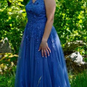 Blå långklänning med spetsdetaljer - Säljer en drömmig blå långklänning med tunna axelband som korsas i ryggen. Klänningen har vackra blommiga spetsdetaljer upptill och ett svepande, transparent lager i kjolen. Perfekt för bal eller student! Materialet känns lätt och elegant. Färgen på bilden är överens med verkligheten. Levereras i klädpåse. 