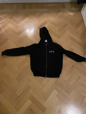 Svart hoodie från Polar Skate Co - Svart hoodie med dragkedja från Polar Skate Co. Liten vit logga på bröstet och stor grafisk logga på ryggen. 