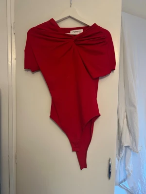 Röd off shoulder body från Pull&bear  - Trendig röd body från Pull & bear med off shoulder-design och snygg twistad detalj framtill. Kortärmad och figurnära passform, perfekt att styla till jeans eller kjol. Mjukt och stretchigt material för en bekväm känsla.