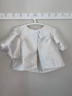 Creme Vit satinblus med puffärmar - Supersnygg creme vit blus från Gina Tricot i glansigt satinmaterial. Blusen har korta puffärmar och en enkel knäppning framtill. Nypris: 500kr