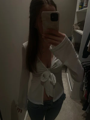 Vit omlottopp med knyt fram - Snygg vit omlottopp med knyt fram och v-ringad design. Långärmad och croppad modell som passar perfekt till jeans. Materialet känns mjukt och lätt, troligen bomull eller polyester. Perfekt för dig som vill ha en trendig och stilren look. Tröjan är från Gina tricot och i stoleken XS.