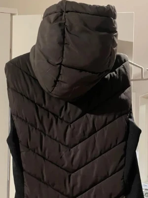 Svart dunväst med huva från Zara - Snygg svart dunväst från Zara st34.  Perfekt för lager på lager och håller dig varm under kyliga dagar. Har inte haft användning av den, den är köpt här på plick men inga synliga tecken på användning