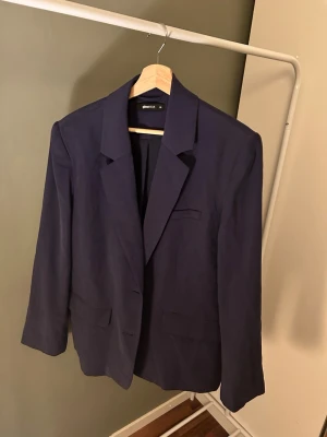 Mörkblå kavaj från Gina Tricot - Stilren mörkblå kavaj från Gina Tricot med klassisk krage och två framfickor. Rak passform och enkelknäppt framtill. Perfekt för en snygg och avslappnad look. Materialet känns mjukt och följsamt. OBS! Kan förekomma katthår på detta plagg därav billigare pris…