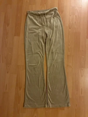 Beige mjukisbyxor med utsvängda ben - Säljer ett par beige mjukisbyxor i mjukt velourmaterial med utsvängda ben. Byxorna har två bakfickor och en relaxed fit som ger en chill vibe. Perfekta för att maxa myset hemma eller till en casual look.