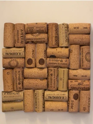 Grytunderlägg av vinkorkar - Ett unikt grytunderlägg gjort av samlade vinkorkar i olika nyanser av beige och brunt. Korkarna är arrangerade i ett kvadratiskt mönster och har tryck från olika vinmärken. Perfekt som dekoration för kök som ger en cool vintouch till rummet.