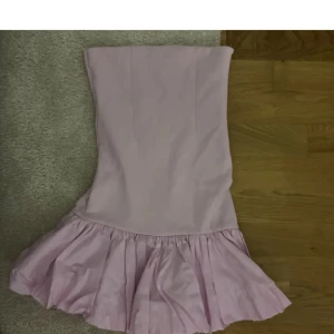 Ljusrosa axelbandslös klänning - Söt ljusrosa klänning med axelbandslös design och volang nertill. Klänningen har en tight passform upptill och är tillverkad i ett mjukt material som ger en feminin look. Perfekt för dig som vill ha en enkel men stylish outfit.