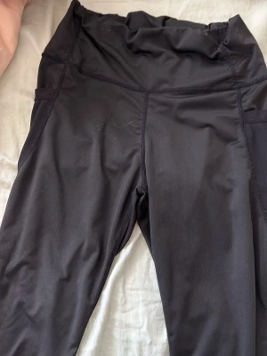 Svarta leggings med hög midja - Säljer ett par svarta leggings med hög midja och bred linning. De har en tight passform och är tillverkade i ett stretchigt material som sitter skönt på kroppen. Perfekta till träning eller chill. Inga synliga loggor eller märken.