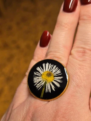 Stor ring med tusensköna - Unik ring med stor rund platta i svart med äkta tusensköna inuti. Perfekt för dig som gillar statement-smycken och blommiga detaljer. Justerbar, i rostfritt stål och små defekt.