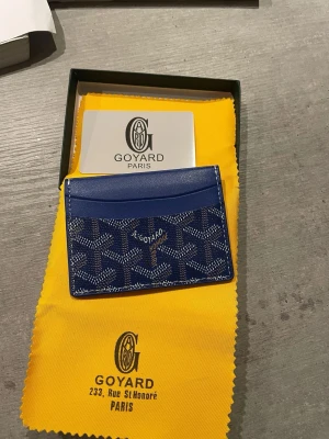 Blå korthållare - Snygg blå korthållare med det klassiska mönstret i vitt och grått. Tillverkad i canvas med läderdetaljer och har flera fack för kort. Perfekt accessoar för dig som vill ha något exklusivt och stilrent.