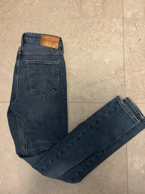 Blå slim fit jeans - Säljer ett par klassiska blå slim fit jeans från Cubus  med snyggt läderpatch bak i midjan. Jeansen har femficksdesign och är tillverkade i bomull med lite stretch för skön passform. Perfekta för dig som gillar en enkel och stilren look. W 29 L 32 