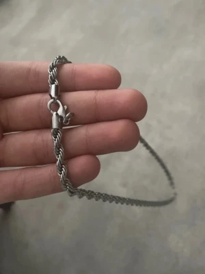  silver kedjehalsband - Säljer ett stilrent halsband i silverfärgad metall med tvinnad kedja och karbinlås. Halsbandet har en chunky känsla och passar perfekt för dig som gillar minimalistiska men ändå iögonfallande accessoarer. Rostfri.