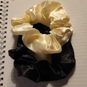 Svart och cremefärgad scrunchie duo - Två scrunchies i glansigt satinmaterial, en i svart och en i cremefärgat. Perfekta för att ge en snygg touch till din frisyr och skonsamma mot håret tack vare det mjuka tyget. Passar både till uppsatt hår och som accessoar runt handleden.