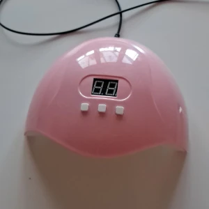 Rosa UV-lampa för naglar - Säljer en söt rosa UV-lampa för naglar med digital display och tre knappar. Den har en USB-anslutning för enkel användning. Perfekt för hemmabruk när du fixar dina naglar.