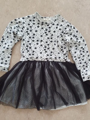 Klänning - Supersöt svartvit klänning med långärmad topp i stjärnmönster och fluffig svart tyllkjol. Perfekt för dig som gillar en lekfull och trendig stil. Toppen är i mjuk bomull och kjolen har flera lager tyll för extra volym.