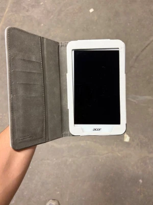 Acer surfplatta med vit fodral - Säljer en Acer surfplatta i ett stilrent vitt fodral med magnetlås. Fodralet har plats för kort och är gjort i ett textilliknande material med grå insida. Perfekt för dig som vill skydda din platta och ha allt samlat på ett ställe.