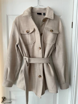 Beige vårjacka Vero Moda -  Vero Moda jacka med knytskärp i midjan och stora bröstfickor, mjukt material.