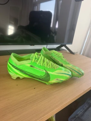 Nike Mercurial gröna fotbollsskor - Säljer ett par Nike Mercurial fotbollsskor i neon-grönt med svarta detaljer och logga. Skorna har låg profil, snörning och mönstrad ovandel för bättre bollkontroll. Sulan har dobbar anpassade för spel på gräs. Perfekta för dig som vill sticka ut på planen.
