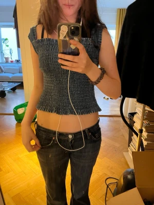 Blå smockad croppad topp - Säljer en blå smockad croppad topp med breda axelband och rynkad struktur. Toppen är ärmlös och har en stretchig passform som sitter tight mot kroppen. Perfekt för dig som gillar en trendig och ungdomlig stil.