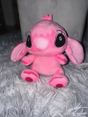 Rosa Angel Stitch gosedjur Disney 20cm - Söt rosa Stitch Angel mjukisdjur i ca 20cm från Disney med stora svarta ögon, långa öron och små detaljer i rött på tassarna. Perfekt som samlarobjekt eller mysig inredningsdetalj för alla som gillar Disney och Lilo & Stitch.