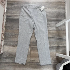 Grå rutiga kostymbyxor H&M - Snygga grå kostymbyxor från H&M med klassiskt rutigt mönster. Byxorna har raka ben och hög midja, perfekta för en stilren look. Materialet är mjukt och bekvämt, och mönstret ger en modern touch till outfiten.