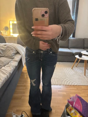 Mörkblå bootcut jeans med slitningar - Säljer ett par mörkblå bootcut jeans med slitningar och snygga kontrastsömmar. Jeansen har broderade detaljer på bakfickorna och en klassisk femficksmodell.  Nästan aldrig använda 