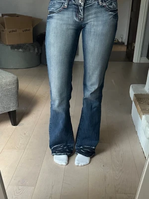 Blå bootcut jeans med slitningar - Säljer ett par blå bootcut jeans med snygga slitningar och tvättade detaljer. Jeansen har låg midja och klassisk femficksdesign. Perfekta för en avslappnad och trendig look. Midja 36 och innerbensläng 79