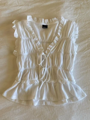 Vit volangblus - Supersöt vit blus från Gina Tricot med volangdetaljer, v-ringning och knyt framtill. Endast Använd en gång