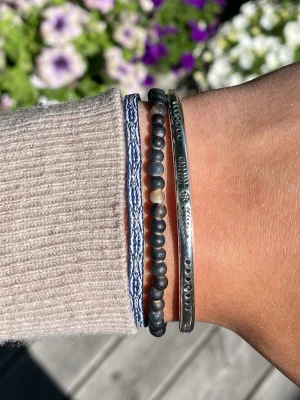 Armbands set - Säljer ett snyggt set med tre armband: ett flätat blåvitt band, ett armband med matta pärlor i svart och grå toner samt ett stelt silverfärgat armband med ingraverade detaljer. Alla armband är justerbara‼️Perfekt för dig som gillar att mixa olika stilar och material. Sälj som ett set. Perfekt till nu till sommaren☀️Skriv om du har några frågor‼️