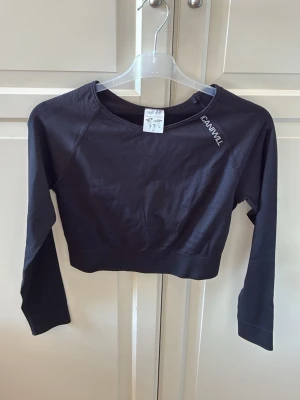 Svart crop top från ICANIWILL - Svart långärmad crop top från ICANIWILL med rund halsringning och logga tryckt vid axeln. Tillverkad i ett stretchigt och mjukt material. Snygg och enkel design som är lätt att matcha med andra träningskläder. Storlek M. I fint skick. 