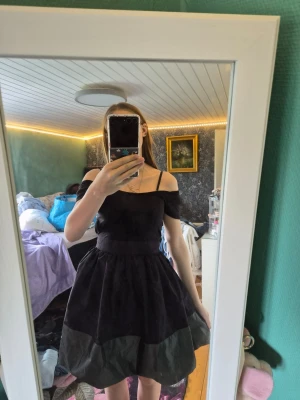 Svart offshoulder klänning från JSFN - Supersöt svart kortklänning från JSFN med offshoulder och smala axelband. Kjolen är utställd och ger en fin siluett. Perfekt för dig som vill ha en stilren och trendig look.