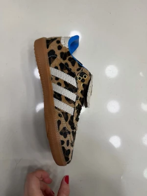 Adidas Wales Bonner leopardmönstrade sneakers(finns i storlek 37-40) - Unika sneakers från Adidas x Wales Bonner med leopardmönstrad ovandel i mocka, vita signaturränder och brun sula. Skon har blått innerfoder och detaljerad plös med logga. Perfekt för dig som vill sticka ut med en djärv stil.