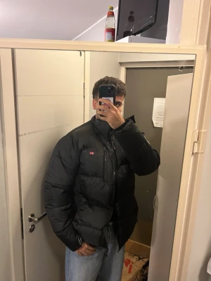 Svart pufferjacka med fuskpäls - Säljer en svart pufferjacka från Norway med huva och fuskpälsdetalj. Jackan har mjukt svart foder, dragkedja och fickor framtill. Perfekt för kalla dagar och riktigt skön att bära. Klassisk pufferstil med lite oversized känsla.
