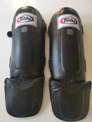 Svarta benskydd Fairtex - Säljer ett par svarta benskydd från Fairtex, perfekta för kampsport som thaiboxning eller MMA. De har kardborreband på sidorna för enkel justering och sitter stabilt på benet. Tillverkade i slitstarkt syntetläder med vaddering för extra skydd.
