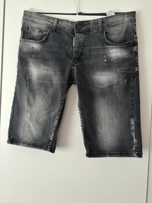 Grå jeansshorts från Dsquared - Snygga grå jeansshorts från Dsquared med slitna detaljer och ljusa partier framtill. Klassisk femficksmodell med knapp och dragkedja. Perfekta för en avslappnad stil under varmare dagar.