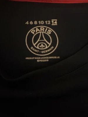 PSG Mbappé matchtröja svart - Snygg svart matchtröja från Paris Saint-Germain med Mbappé och nummer 7 på ryggen. Tröjan har klubbens officiella logga tryckt på insidan och är tillverkad i ett lätt och bekvämt material som passar perfekt till fotbollsträning eller som supporterplagg.
