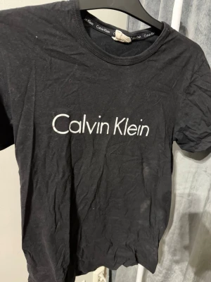 Svart Calvin Klein t-shirt - Svart t-shirt från Calvin Klein med klassisk vit logga tryckt på bröstet. Rund halsringning och korta ärmar. Tillverkad i mjukt material som känns skönt mot huden. Perfekt för en stilren och enkel look.