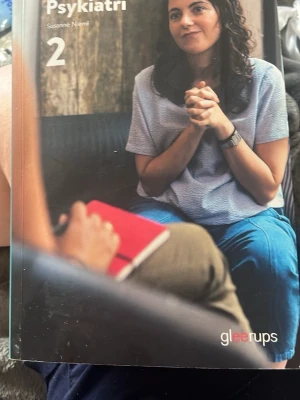 Psykiatri 2 kursbok Gleerups - Kurslitteratur i psykologi, 'Psykiatri 2' av Susanne Niemi. Boken har ett mjukt omslag i gröna och grå toner med ett foto på framsidan. Perfekt för dig som läser vård- och omsorgsprogrammet eller vill fördjupa dig i psykiatri.