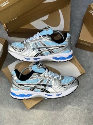 ASICS sneakers i blått och silver - Snygga ASICS sneakers med mesh i ljusblått, detaljer i silver och svart samt vita och blå inslag på sulan. Skorna har klassisk snörning, sportig vibe och ikoniska ASICS-ränder på sidorna. Perfekta för dig som gillar streetstyle och sportig look.