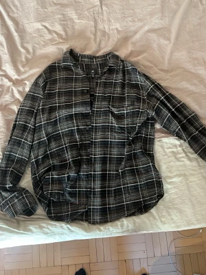 Svart och vit rutig skjorta H&M - Klassisk svart och vit rutig skjorta från H&M med lång ärm och bröstficka. Skjortan har knappar framtill och är tillverkad i mjuk bomull. Perfekt för en avslappnad och stilren look.