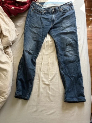 Blå Levi's raka jeans - Klassiska blå jeans från Levi's med rak passform och fem fickor. Jeansen har en mörkblå tvätt, orange sömmar och läderpatch bak i midjan. Tillverkade i slitstark denim, perfekta för en avslappnad och tidlös stil. Modell 511. Storlek 36/34 men har blivit uppsydda till 36/32. Nytt pris ca 1100, mitt pris 249