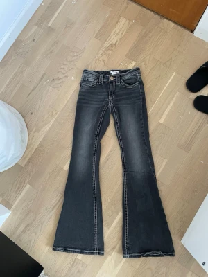 Svarta utsvängda jeans Gina Tricot - Snygga svarta jeans från Gina Tricot med utsvängda ben och markerade vita sömmar. Jeansen har klassisk femficksdesign och knappstängning framtill. Perfekta för dig som gillar en trendig och avslappnad stil.