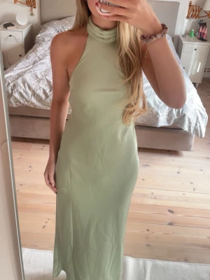 Ljusgrön långklänning med snörning - Snygg ljusgrön långklänning med halterneck och öppen rygg med snörning. Klänningen har en tight passform och är ärmlös, perfekt för sommarens alla tillfällen. 